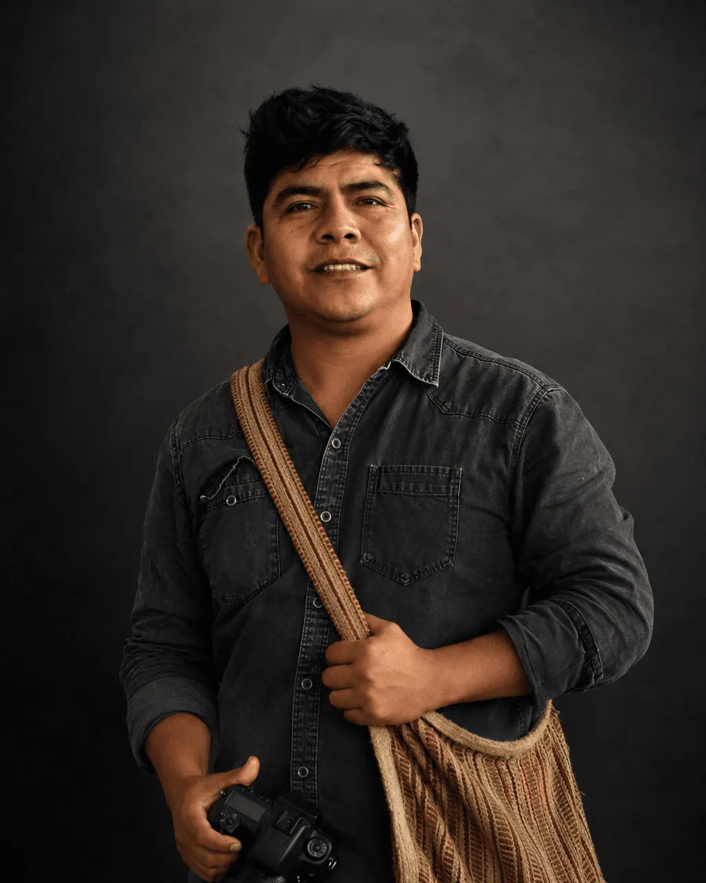 Retrato de Carlos Ayasta en estudio, con su cámara en la mano y una alforja de fibra al hombro