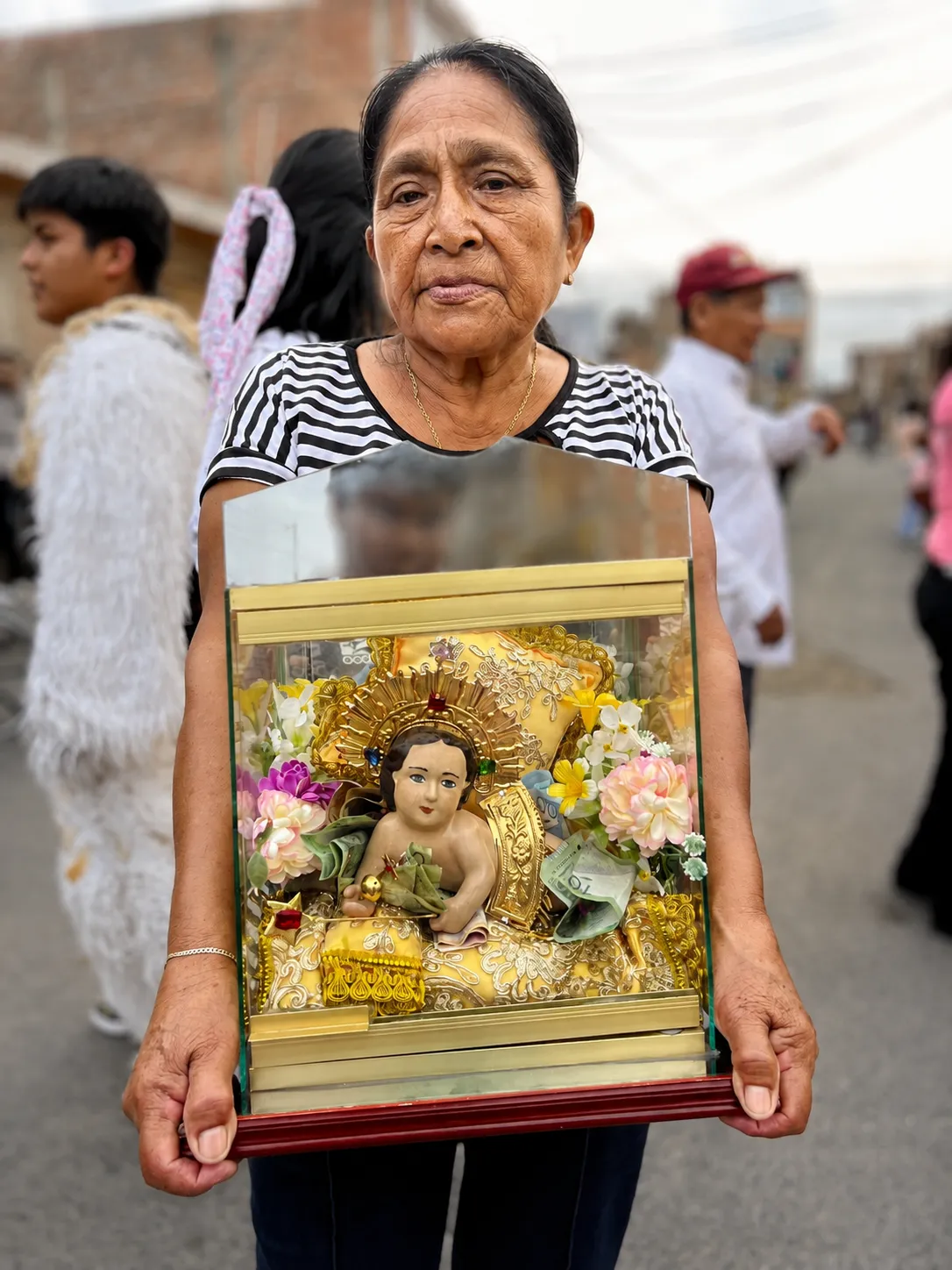 Mujer sostiene frente a su pecho una urna pequeña con una imagen religiosa