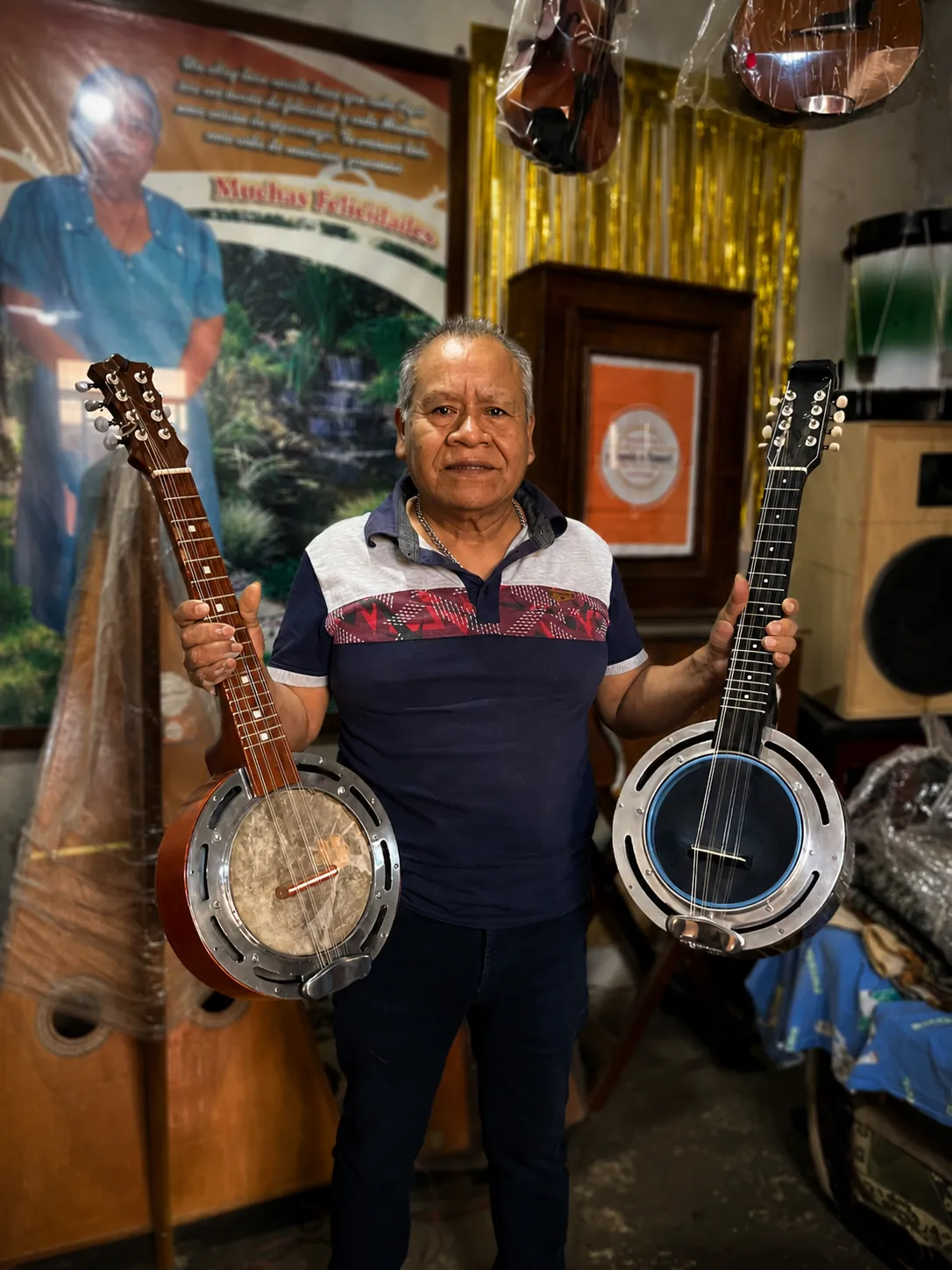 Hombre de pie en un taller sosteniendo dos instrumentos de cuerda