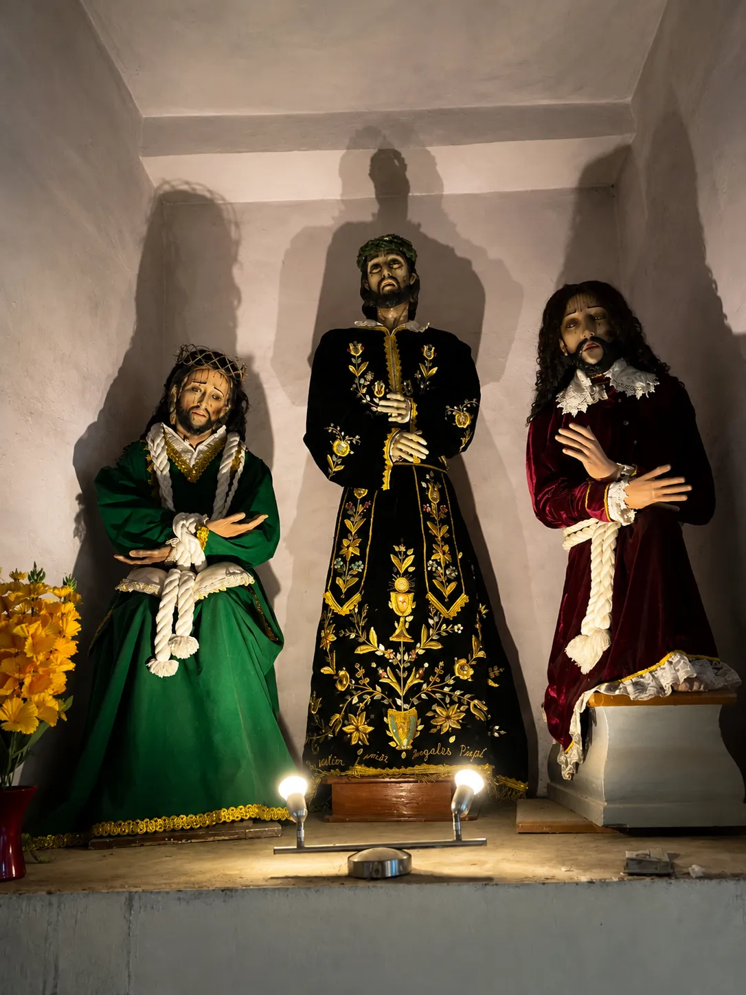 Tres imágenes religiosas vestidas dentro de una hornacina blanca