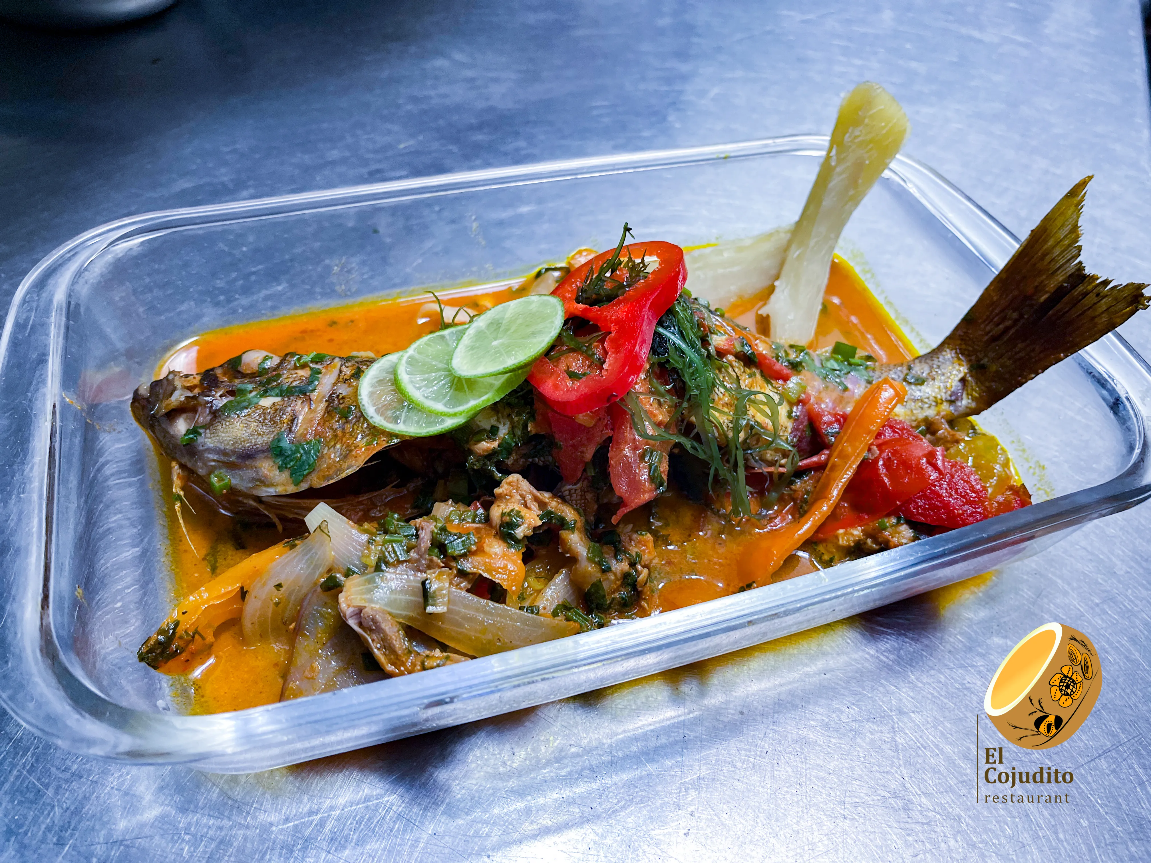 Pescado entero en una fuente transparente con salsa, cebolla, pimiento y hierbas